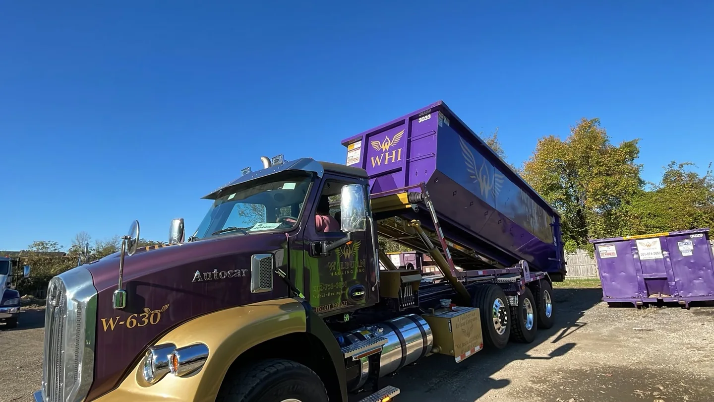 Purple and gold Wilburn Hauling Autocar roll-off truck carrying a branded container